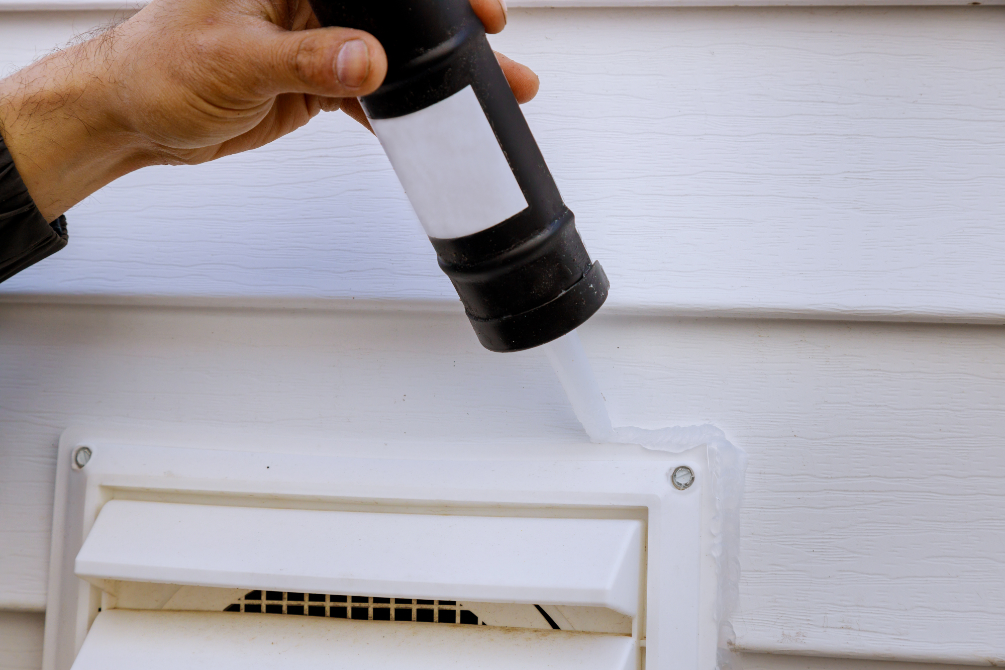 Person caulking around the edges of a exterior house vent